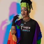 Person wearing a colorful jacket and black shirt with text, standing against a multicolored background