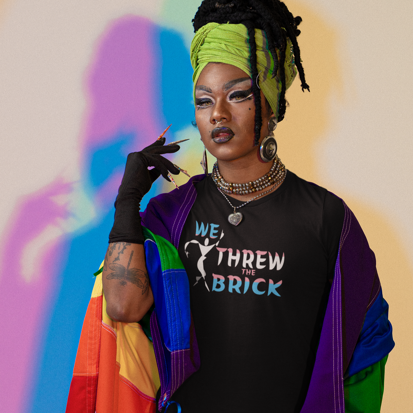Person wearing a colorful jacket and black shirt with text, standing against a multicolored background